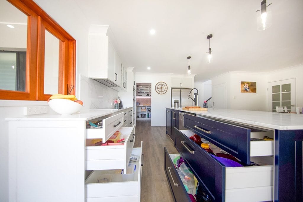 View of open long blue sliding kitchen drawers under island bench