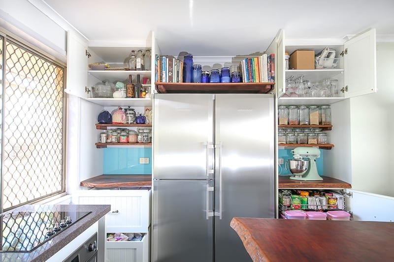 Three door stainless steel fridge with overhead storage shelves and cupboards