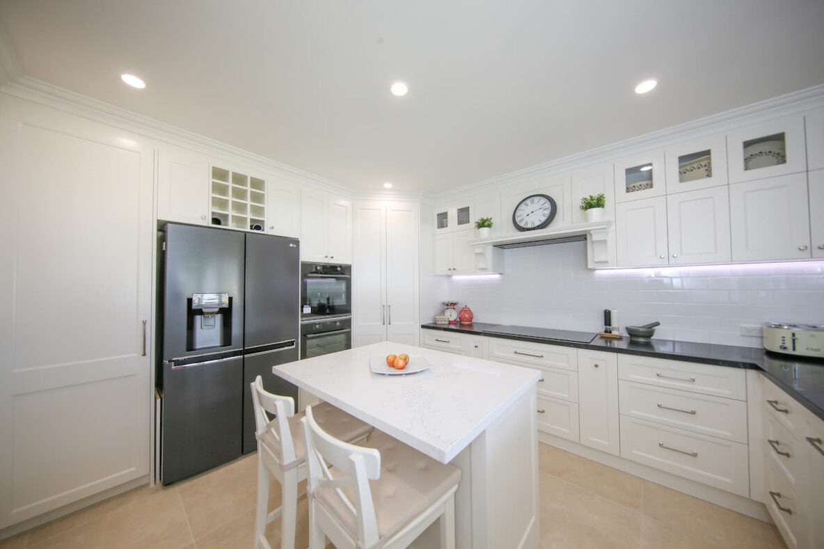 white Hampton style kitchen cabinetry with black granite benchtop against white subway tiles with LED lighting strip