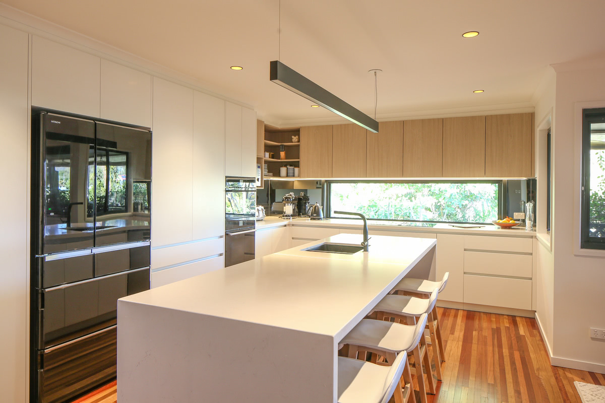 renovated kitchen with white waterfall island bench statement lighting and wooden floors